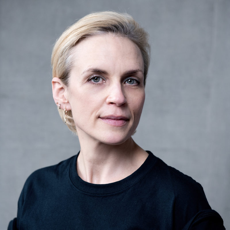 Caroline Lofthouse. A headshot of a smiling person with short blonde slicked back hair