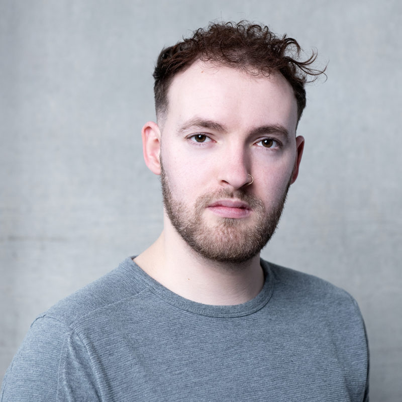 Ted Wilkinson. A headshot of a person wearing a grey tshirt and short brown hair and stubble
