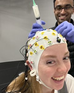 A person fitting an EEG (electroencephalography) cap with wires onto our dancer's (Paulina Porwollik) head to measure brain waves during a dance session. Both are smiling joyfully.