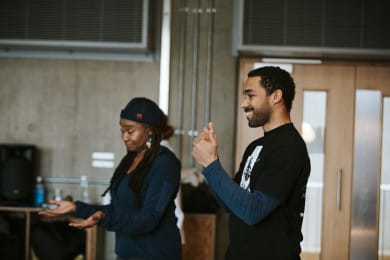 Two people standing in a studio facing to the left. Both are gesturing. We can see only their top halves.